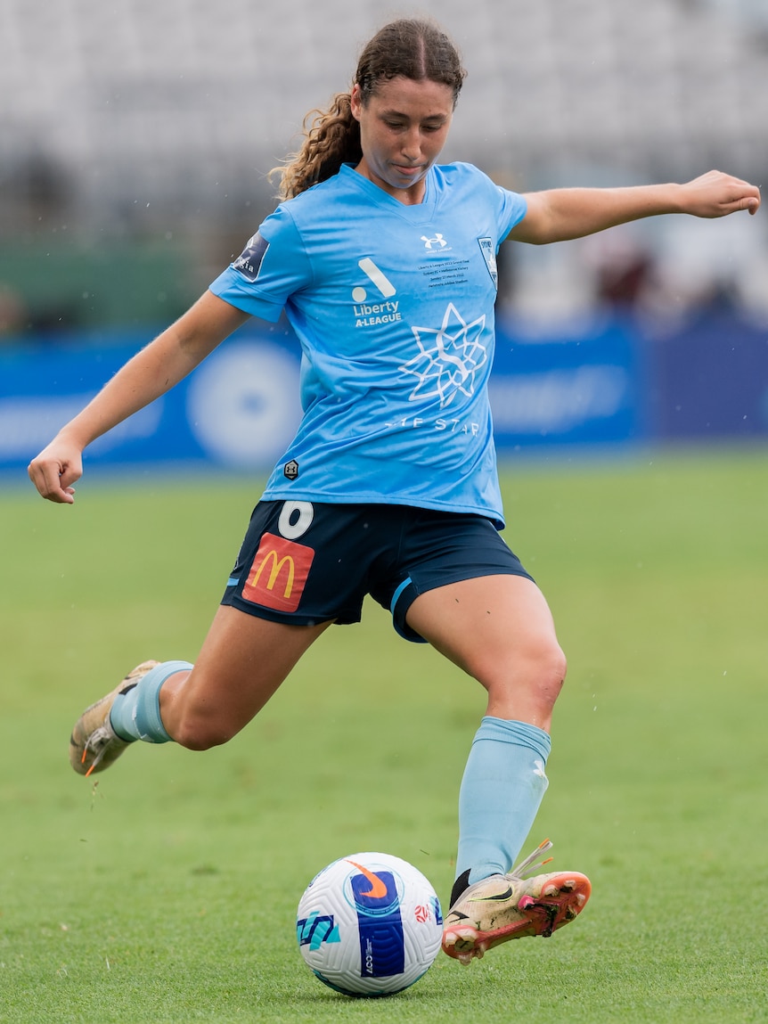 A female soccer player wearing blue kicks a ball