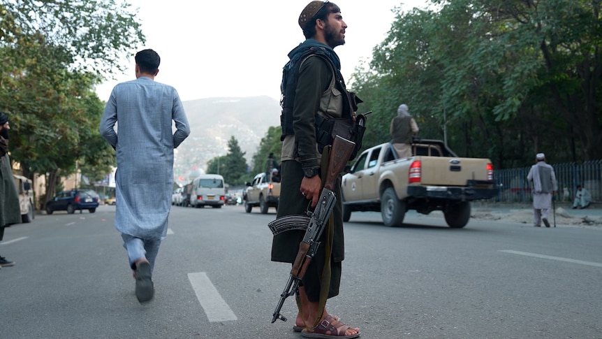 A man stands in the middle of a street holding a machine gun.