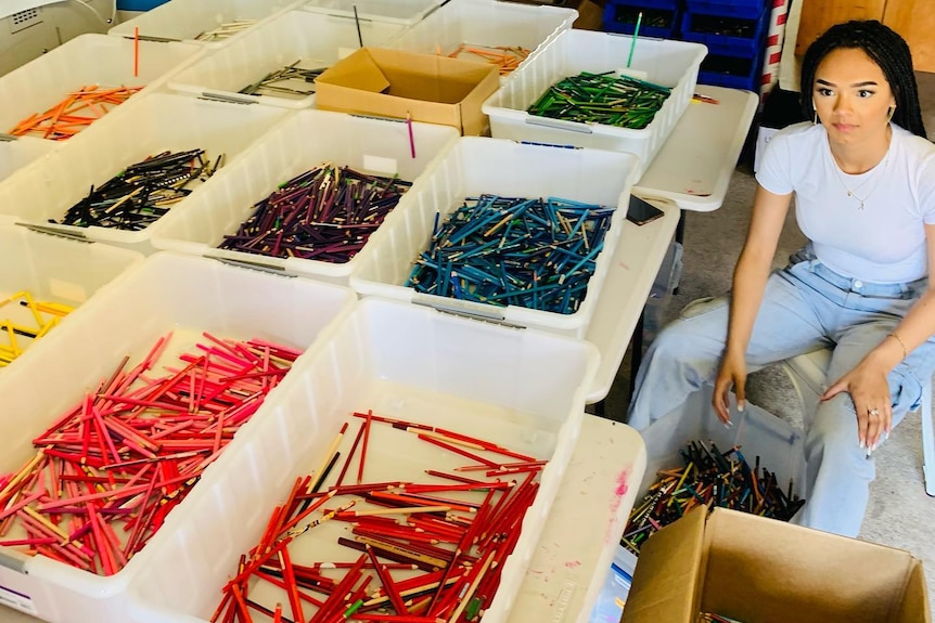 A woman in jeans and white shirt sorting coloured pencils into boxes.