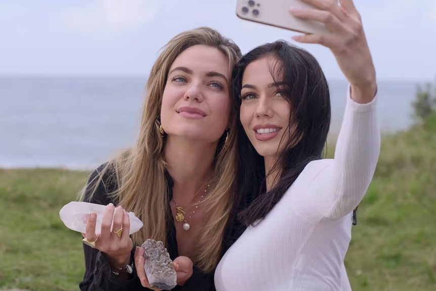 To women take a selfie on an iphone. One is holding crystals. 