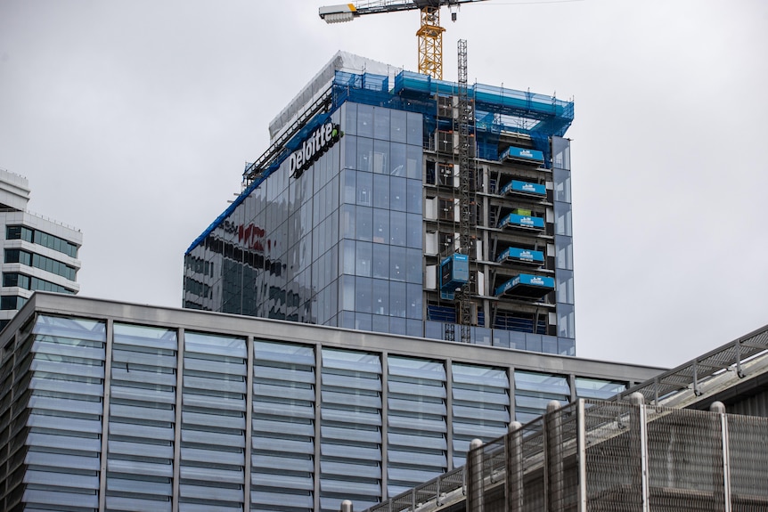 A tall glass building that is being constructed with a crane in the middle. 
