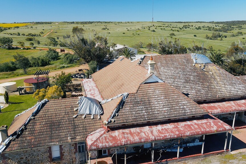 An aerial photo of the damaged roof of an old homestead. It is covered in tarps. 