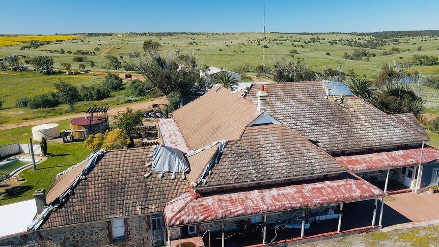 An aerial photo of the damaged roof of an old homestead. It is covered in tarps held down by sandbags 