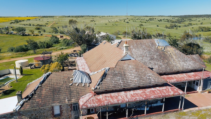 An aerial photo of the damaged roof of an old homestead. It is covered in tarps held down by sandbags 