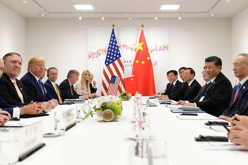 Looking down a bright white conference table, American and Chinese dignitaries are seated opposite each other.