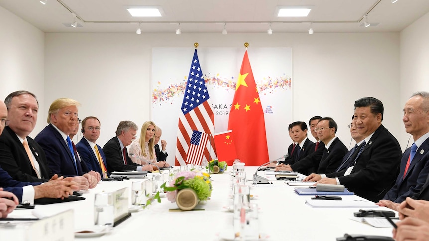 Looking down a bright white conference table, American and Chinese dignitaries are seated opposite each other.
