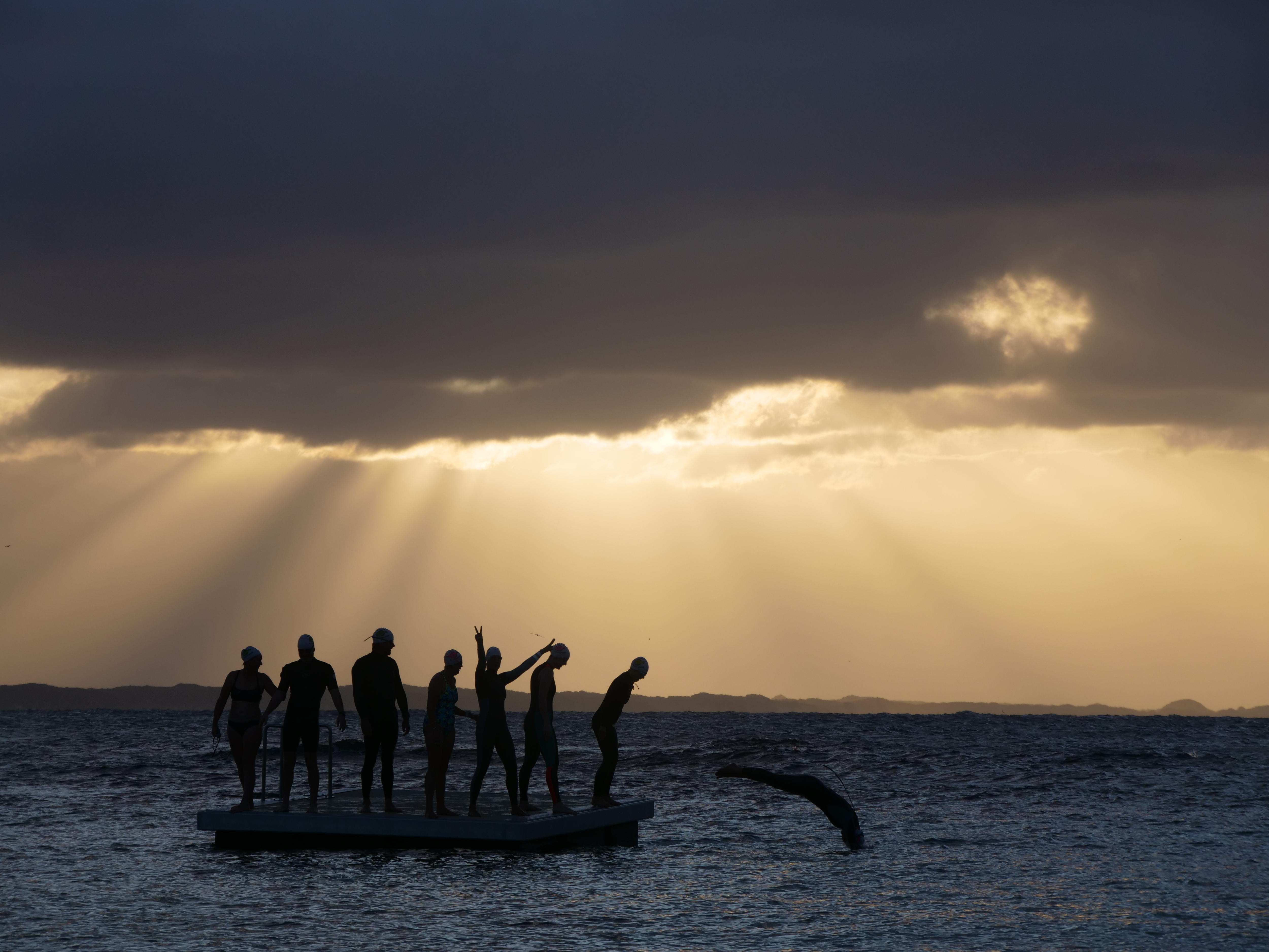 A group of swimmers on a pontoon at sunrise.
