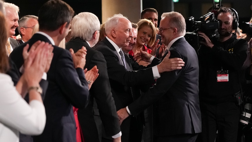 Albanese shakes Keating's hand, as Keating pats his back, with the pair surrounded by a large crowd.