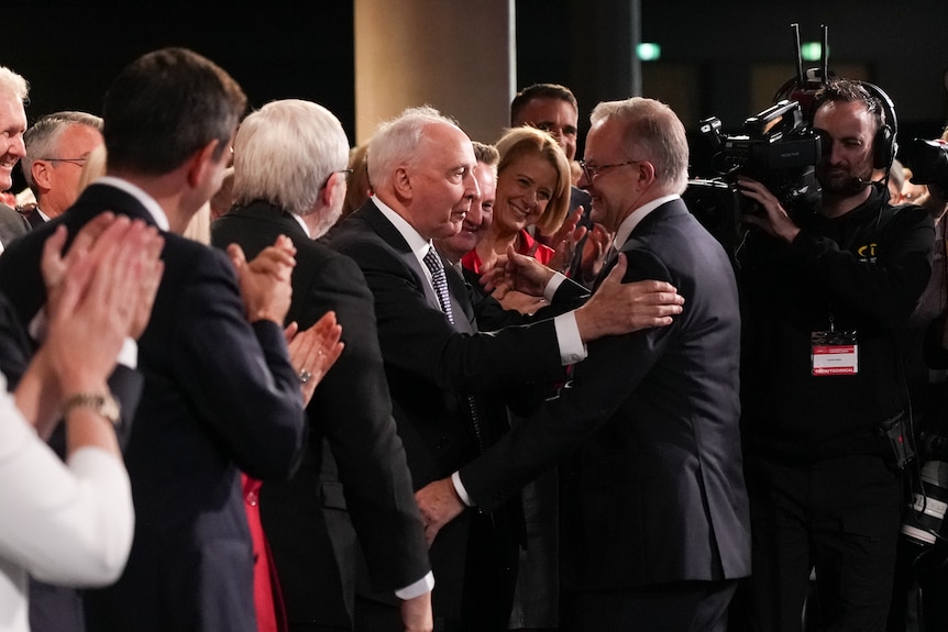 Albanese shakes Keating's hand, as Keating pats his back, with the pair surrounded by a large crowd.