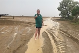 Man in shorts and a green shirt stands barefoot in soaked ground pointing thumbs up at camera