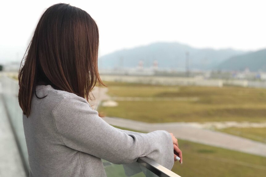 'Chloe' stands on a balcony, looking out to the airport.