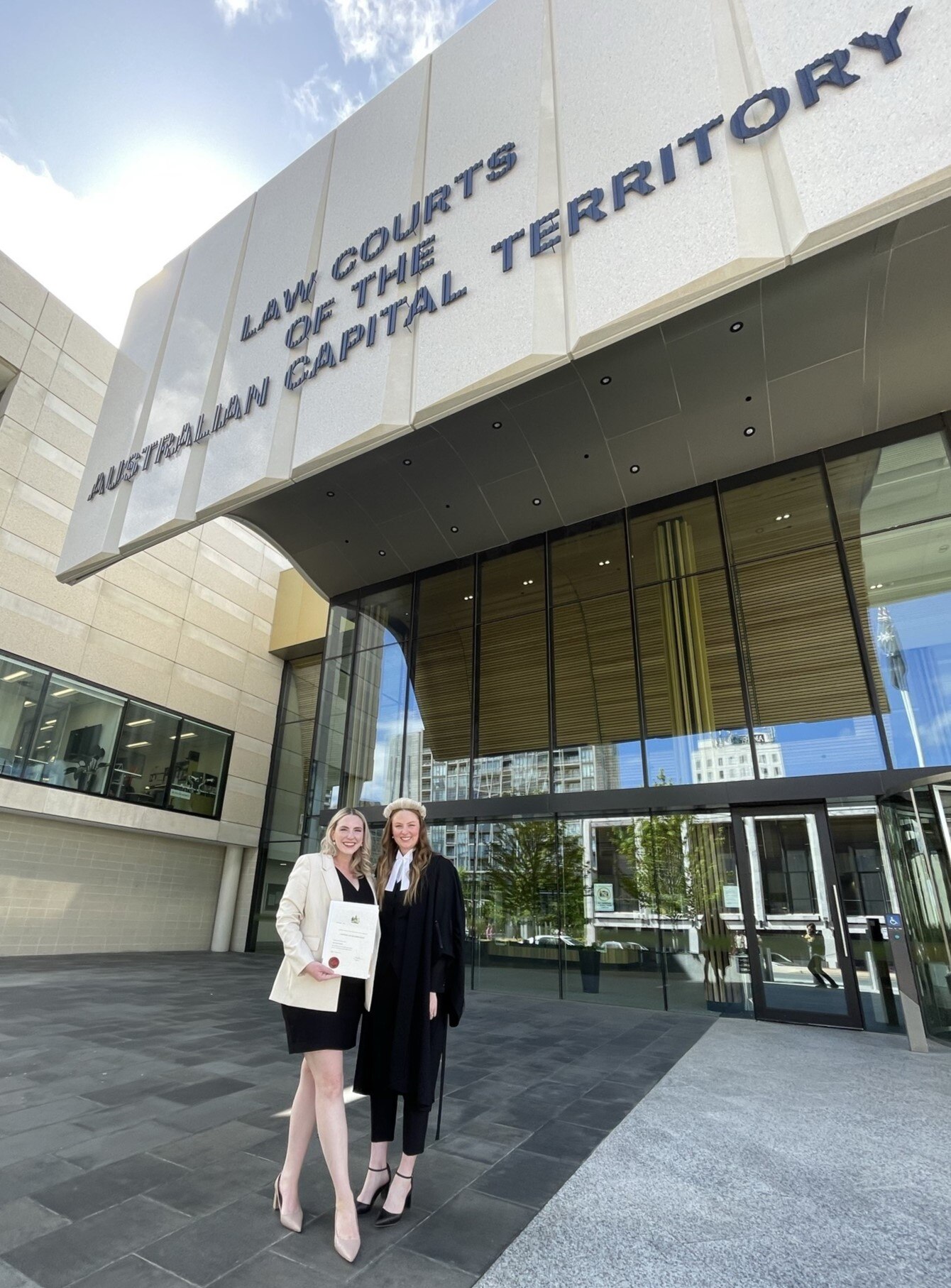 Two women stand smiling in front of the Law Courts of the Australian Capital Territory