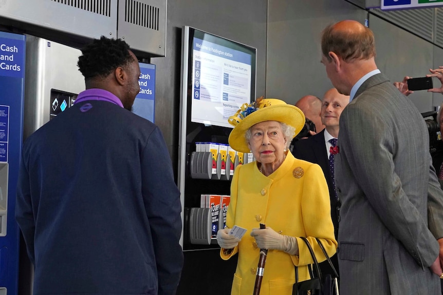 Queen Elizabeth II looks at Prince Edward at a ticket machine