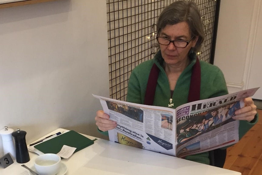 Woman across cafe table reading a newspaper