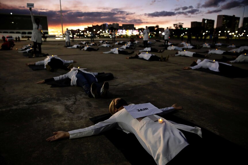 Nurses lay on the ground dressed in white coats with signs of names displayed on their stomachs.