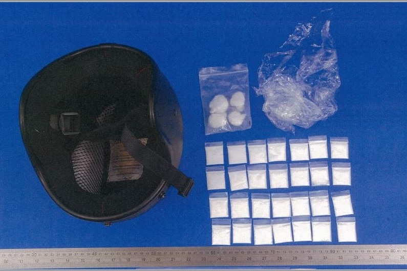 black motorbike helmet next to bags of cocaine on blue background