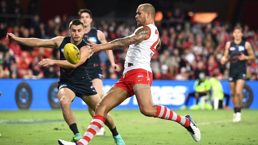 A Sydney Swans AFL player tries to kick the ball while under defensive pressure from a Giants player.