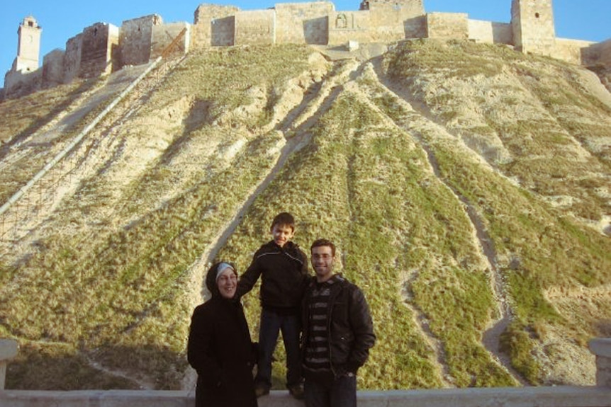 Amina with her son Majd and grandson stand in front of ancient fortified walls in Aleppo's old city.