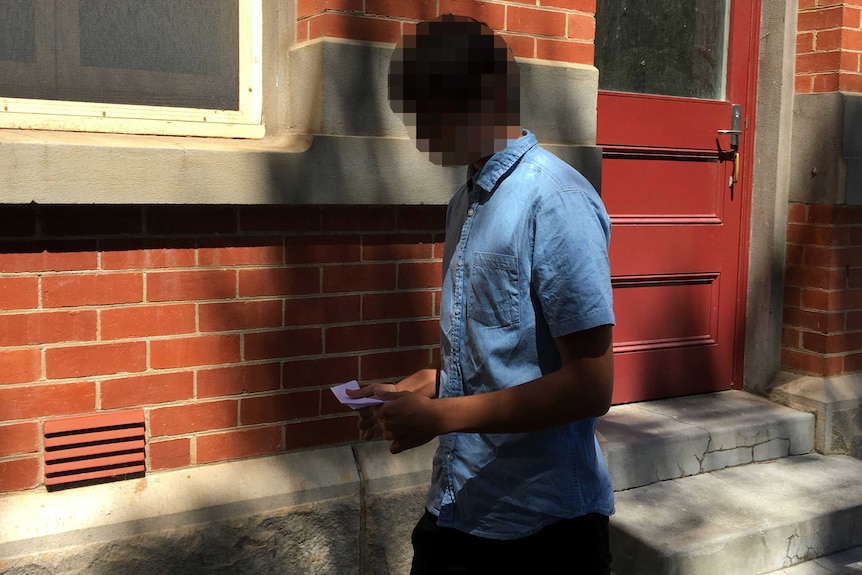 A boy wearing a blue shirt and black trousers with his face pixellated walks along a path outside the Supreme Court in Perth.