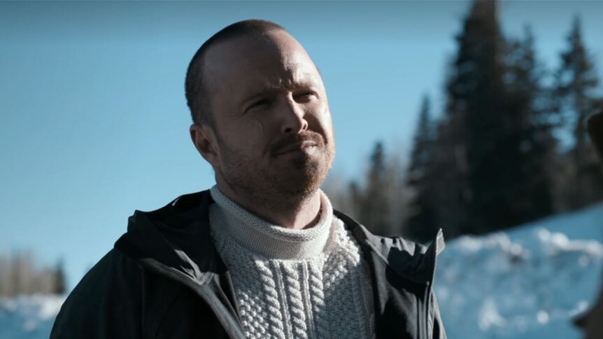 A man squints while rugged up in the Alaskan wilderness with snow on the ground.