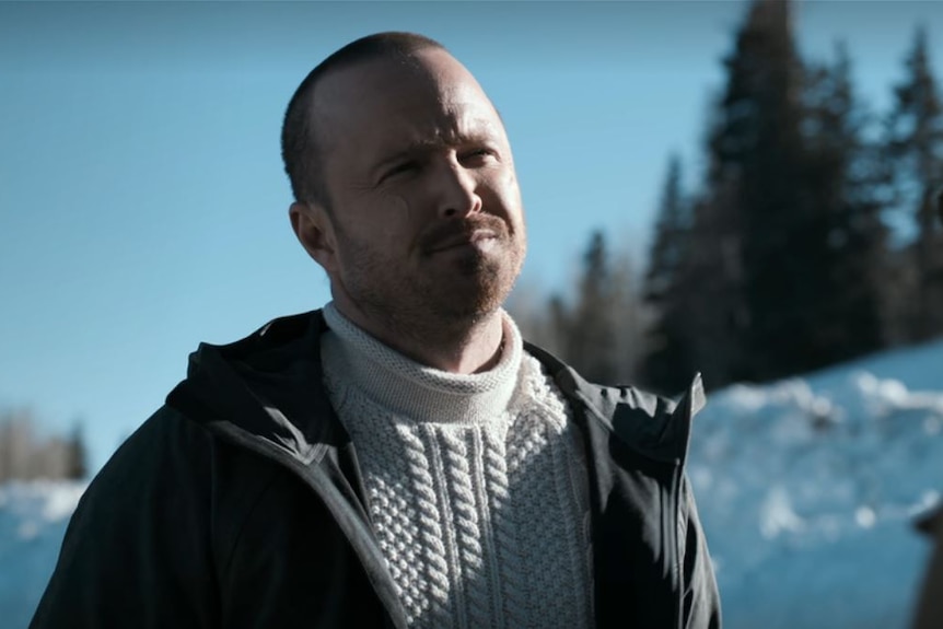 A man squints while rugged up in the Alaskan wilderness with snow on the ground.