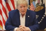 Donald Trump sitting at a desk, facing the camera.