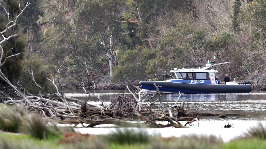 A boat on the Swan River with thick trees either side and branches in the water in the foreground.