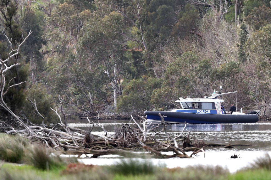 A boat on the Swan River with thick trees either side and branches in the water in the foreground.