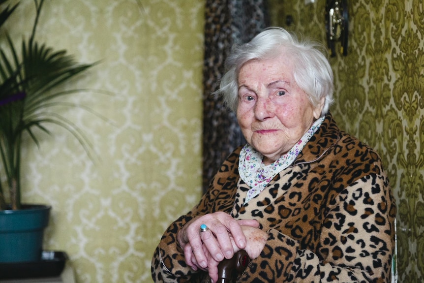 Valeria Miller sits in a room with green wallpaper and looks into the camera with a grin