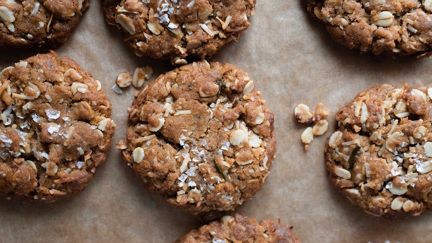 A tray of baked Anzac biscuits on baking paper topped with sea salt, a classic Anzac Day baking project.