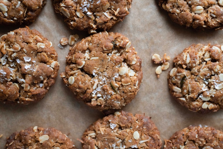 A tray of baked Anzac biscuits on baking paper topped with sea salt, a classic Anzac Day baking project.