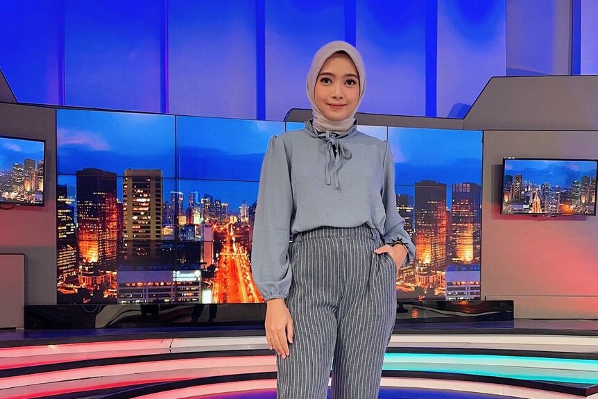 A full-length photos of a woman in a headscarf in a news studio.  