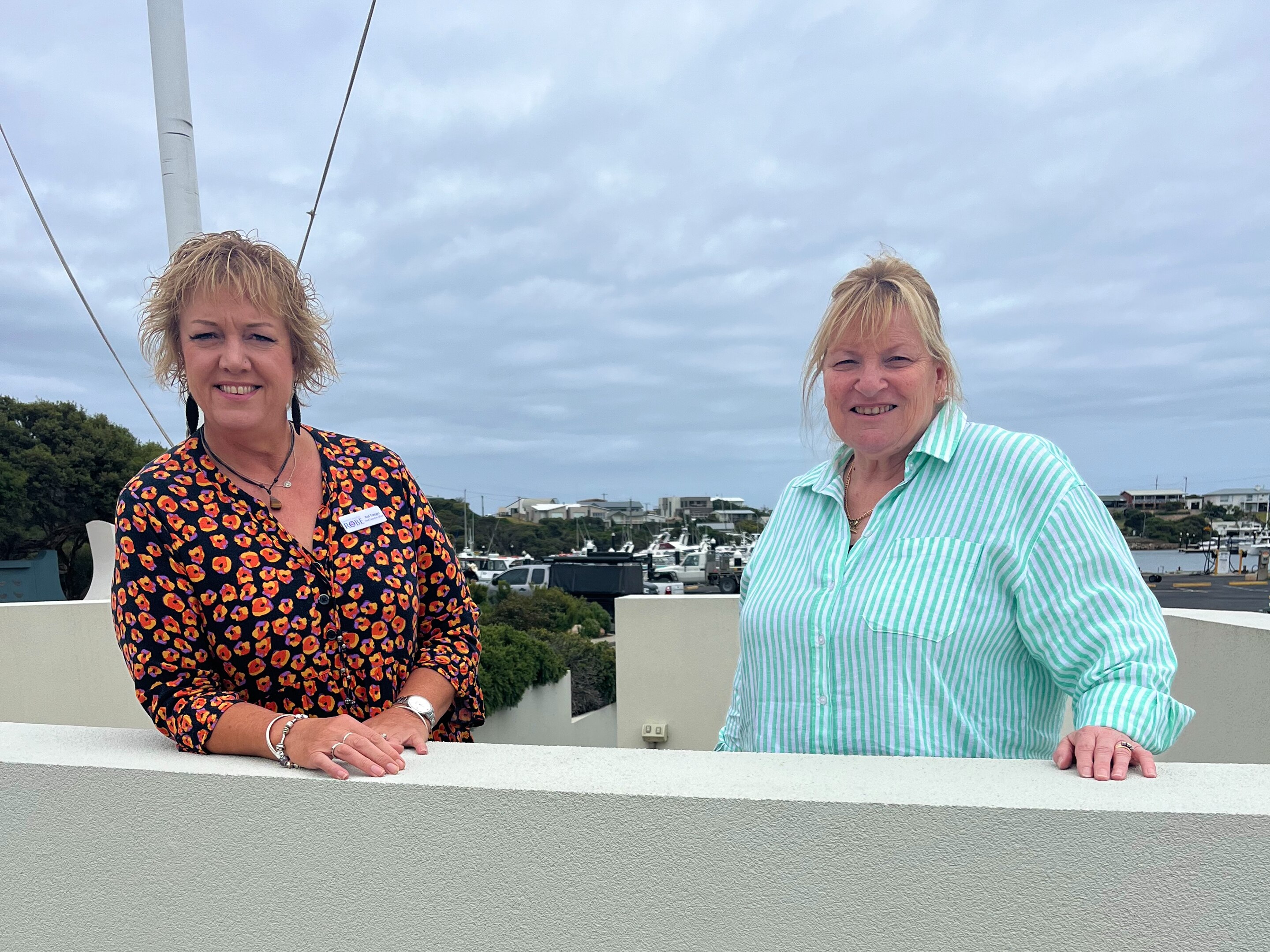 Two women smiling standing behind a short fence
