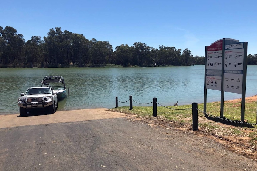 A four-wheel drive is parked at the edge of a river and puts a boat into the water.