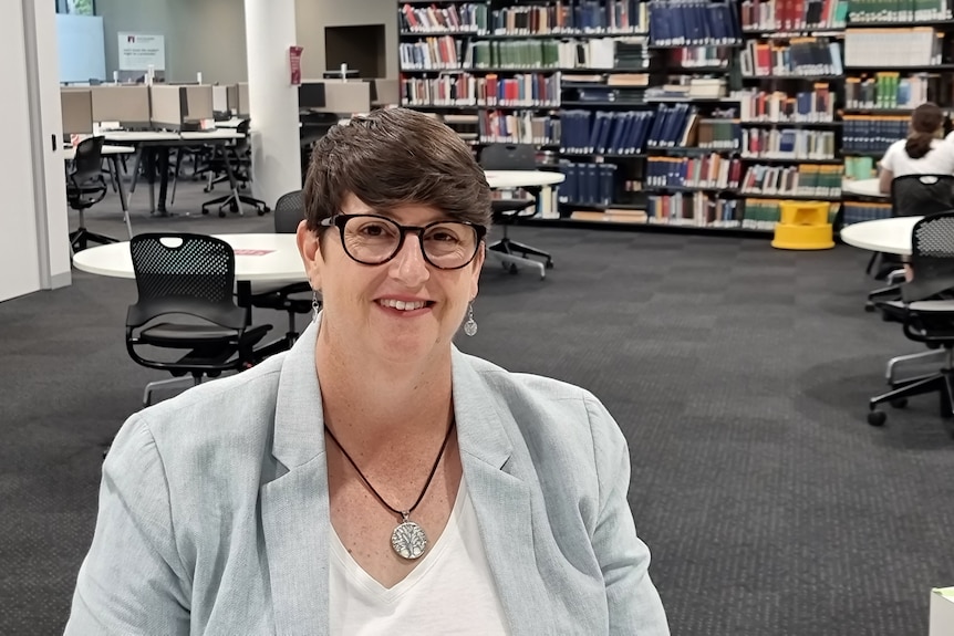 Woman sitting in a library wearing a light blue blazer and white shirt.