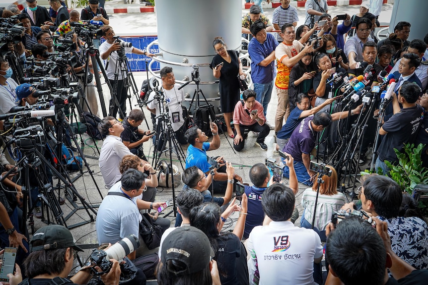 A huge scrum of reporters, camera operators and photographers face towards one man behind many microphones