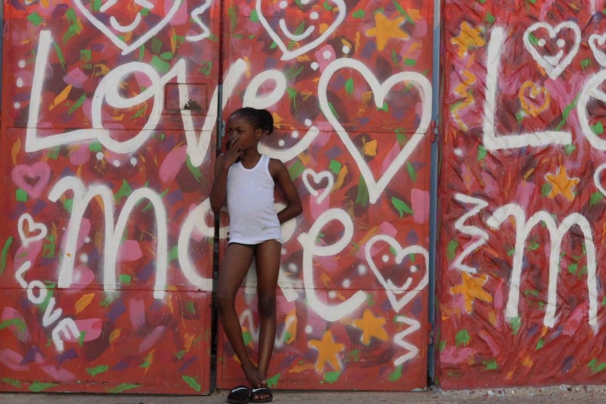 A young girl stands in front graffiti in Trench Town Jamaica.