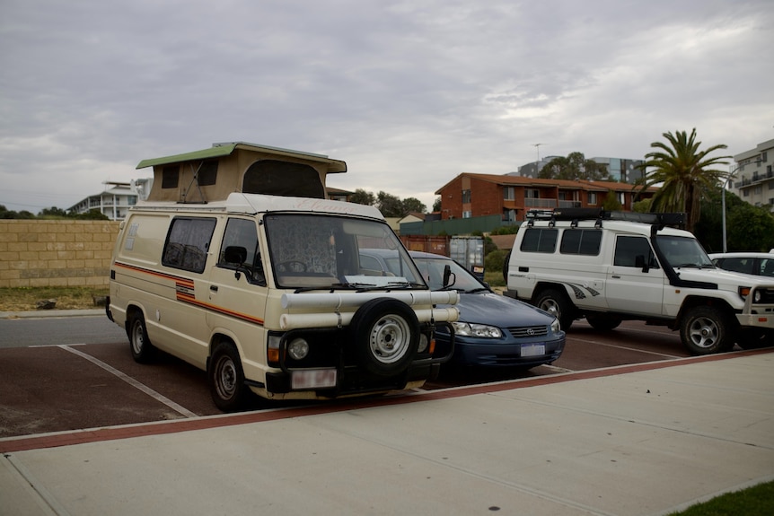 An old, small campervan parked in a car park at Scarborough Beach, with other vehicles to the right.
