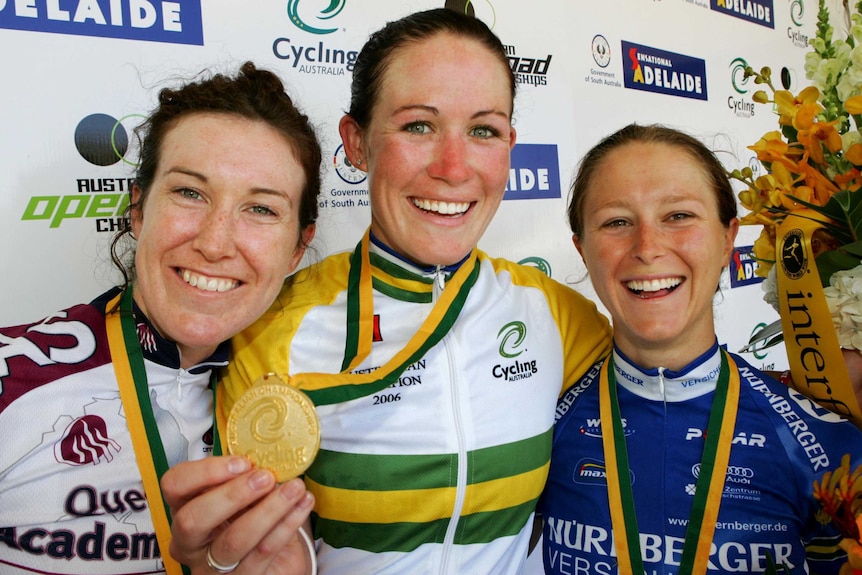 Kate Bates and two other women stand arm in arm and smile with medals around their necks