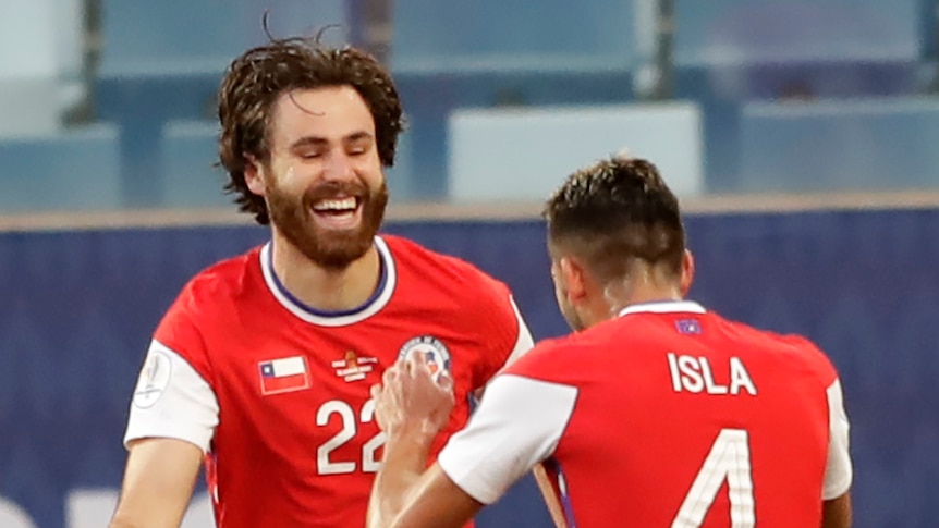 Chile teammates congratulate a smiling man with a beard.