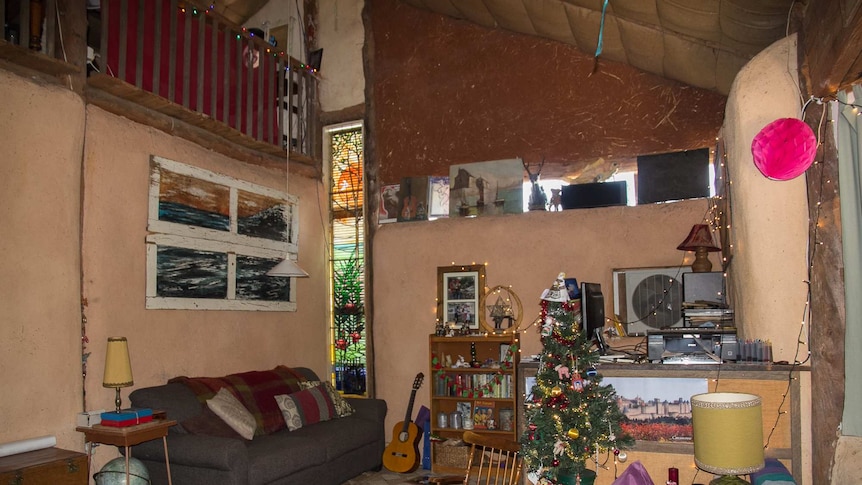 Inside of a lounge room of a straw bale house with exposed poles and straw