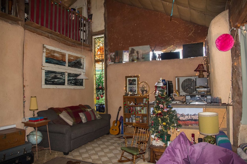 Inside of a lounge room of a straw bale house with exposed poles and straw