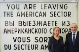 Mikhail Khodorkovsky and Alexandra Hildebrandt stand in front of a sign that says "YOU ARE LEAVING THE AMERICAN SECTOR".