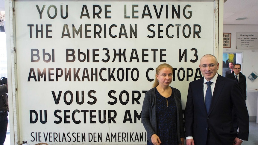 Mikhail Khodorkovsky and Alexandra Hildebrandt stand in front of a sign that says "YOU ARE LEAVING THE AMERICAN SECTOR".