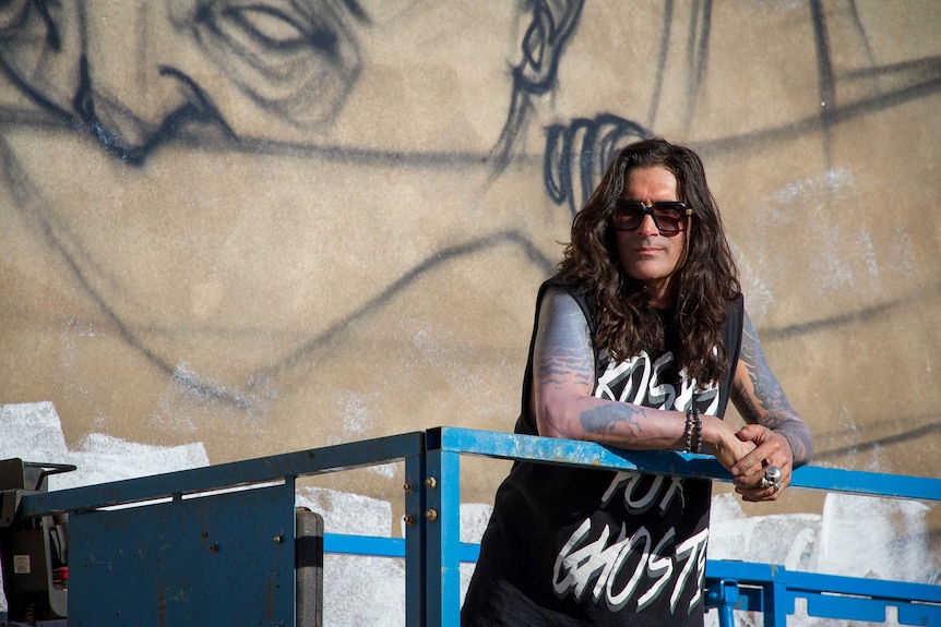 Artist Stormie Mills poses in front of his work in Kalgoorlie