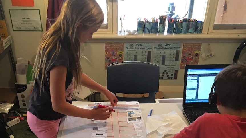 A girl and her brother do school lessons at their home.