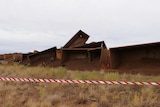 Red and white tape blocks off the scene where a rust-coloured train derailed in outback scrub.
