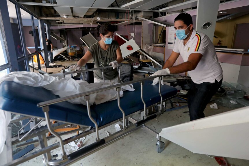 People wearing face masks move a gurney at a damaged hospital.