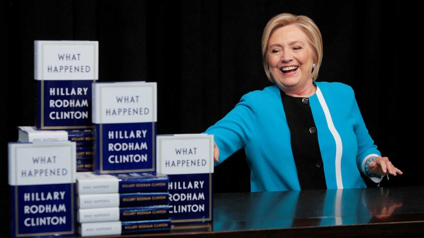 Hillary Clinton flashes a toothy grin as the grabs a book to sign at her book tour.