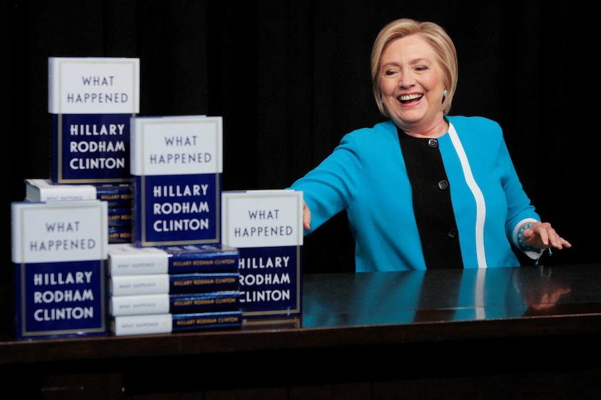 Hillary Clinton flashes a toothy grin as the grabs a book to sign at her book tour.